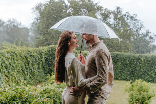 Smiling couple standing with umbrella in rain at garden