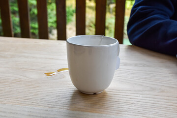 White ceramic mug with tea on wooden table. Green tea bag. Spilled tea on the table. Terrace with seating
