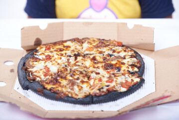 Black pizza with Italian salami sausage, mozzarella cheese and ham