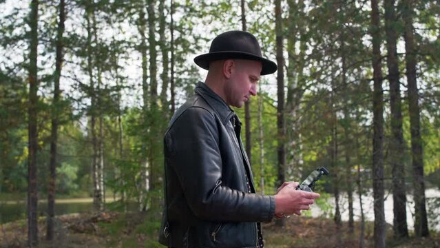 Caucasian model operating a drone in the forest and looking to his device. Wide shot