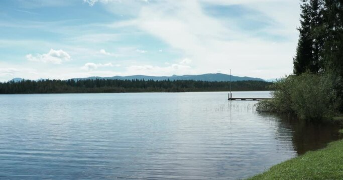 The Calm bog waters of Kirchsee near Sachsenkam and Bad T&ouml;lz nearby the Kloster Reutberg monastery along the Zeller Forest with view on the jetty of lifeguard station and Bavarian Alps on horizon
