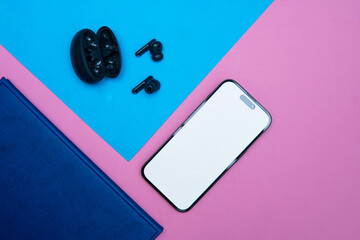 flat lay photo showing a phone next to wireless headphones and a notebook. Concept showing listening to e-books or podcasts