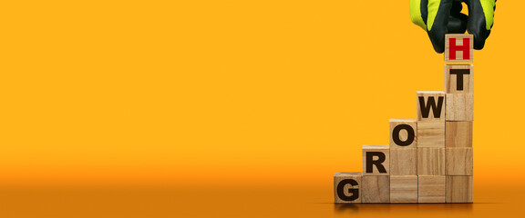 Gloved hand arranging wood blocks with text Growth on an orange and yellow background with copy...