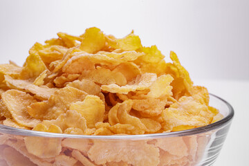 cornflakes in the foreground inside a glass bowl on a white background