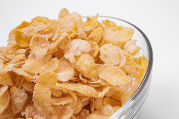 cornflakes in the foreground inside a glass bowl on a white background