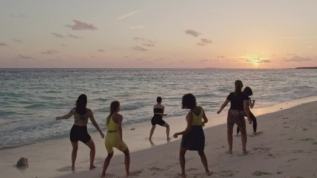 Group of professional dancers having a rehearsal on Maldivian beach at sunset. Aerial Drone shot flyover. High quality slow motion 4k footage.