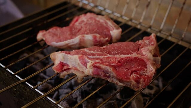 Preparazione alla Griglia: Cuoco che Posiziona Bistecche di Manzo Crude su Carbonella Fumante in Primissimo Piano