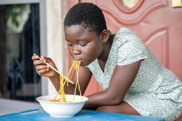 image of young black girl eating noodles with chopstick- african kid enjoying asian delicacy- food...