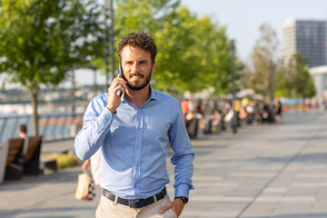 Business man walking along the sidewalk talking on the smartphone - obrazy, fototapety, plakaty