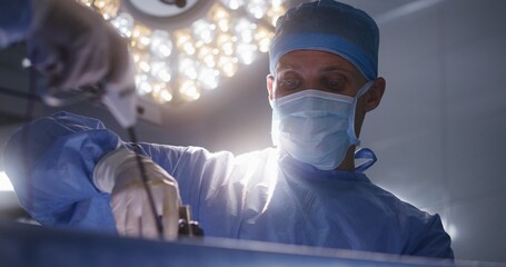 Close up of adult male medic assisting surgeon during surgery. Professional doctors operate patient...