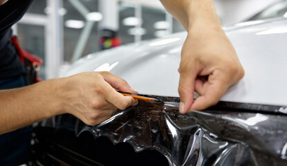 Car detailing specialist putting vinyl foil or film on car hood closeup