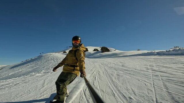 Man snowboards in breathtaking mountain backcountry. Extreme snowboarder shreds powder while carving snow at fence that prevents falls on prepared ski run. Cinematic shot of snowboarder