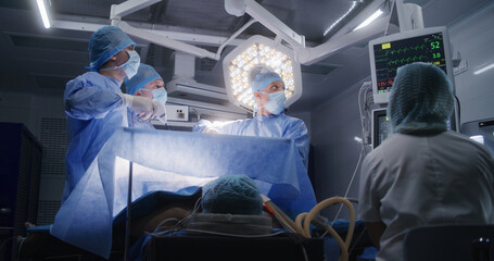Nurse checks condition of patient on electrocardiography monitors. Adult man lies under anesthesia...