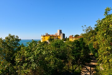 Obraz premium Trail leading through a mediterranean forest and Duino castle behind in Duino-Aurisina, Italy