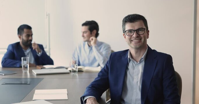 Mature confident good-looking company boss, office employee sit at desk with staff members smile look at camera, feel satisfied by company position and career growth. Portrait of corporation founder