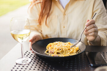 Caucasian young woman eating pasta carbonara and drinking white wine. Concept of italian lifestyle....