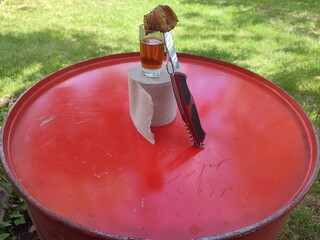 a glass of cognac stands on a red iron barrel along with a roll of toilet paper with a folding iron...