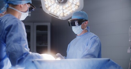 Team of surgeons in protective glasses use laparoscopic tools during surgery. Doctors and...
