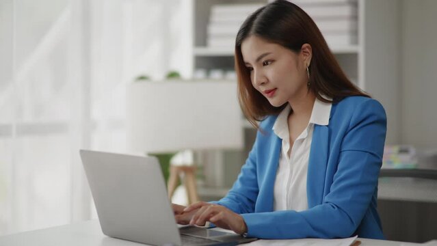 Businesswoman in blue suit is working on laptop with happy face in office space.