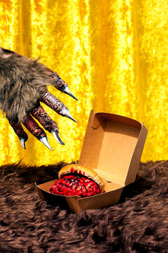 Unrecognizable monster taking bloody brain burger from box