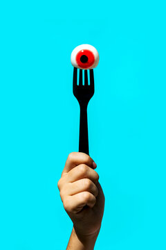 Unrecognizable person with eyeball on fork against blue background