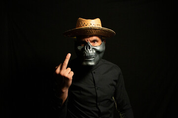 Adult man dressed in black with skull mask and straw hat on a black background in a scary concept