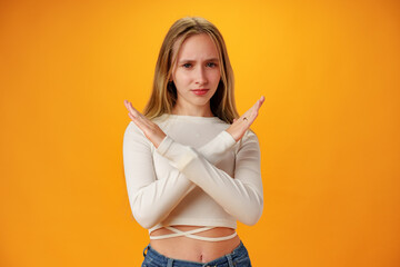 Teen girl shows cross hands gesture, rejecting something over yellow background in studio