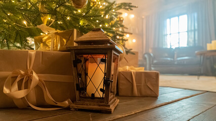 Vintage lantern with candle and gifts near Christmas tree at home closeup. Old fashioned lamp with presents under decorated fir tree in living room. Happy winter holidays interior design