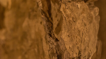 Old textured rocks in wall structure at orange light closeup. Rough boulders with pattern used in building construction works. Stone material put in house foundation at warm light