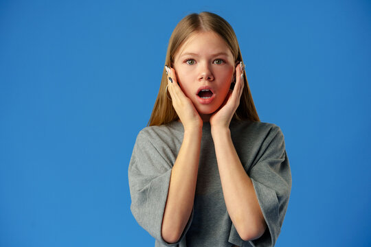 Surprised amazed teen girl against blue background in studio