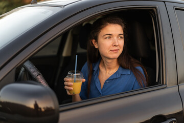 Happy woman driver stops to relax drinks orange juice, enjoy the journey