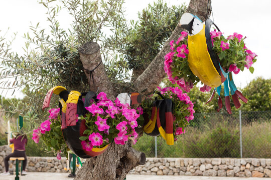 Colorful parrot decorations, hanging on the tree, made with car tires and pink petunias on "Costitx en Flor" (Costitx in bloom) Flower Fair, Majorca, Spain