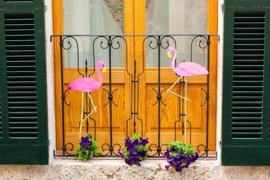 Door with green shutters, decorated with two pink flamingos and some flower pots with violet petunia on "Costitx en Flor" (Costitx in bloom) Flower Fair, Majorca, Spain