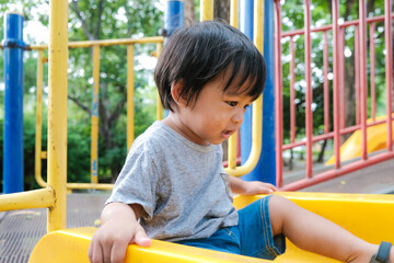 Happy preschool asian boy enjoying with outdoor slider in city park playground