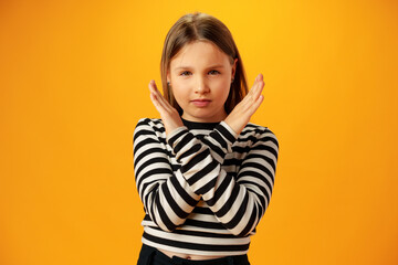 Teen girl shows cross hands gesture, rejecting something over yellow background in studio
