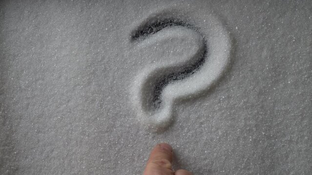 Hand drawn question mark on a background of white sugar. Question mark written on white sugar background, top view, close up