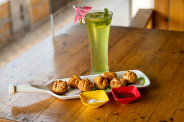 Vegetable fried momo with sauce served and Green apple mojitho mocktail over a rustic wooden background