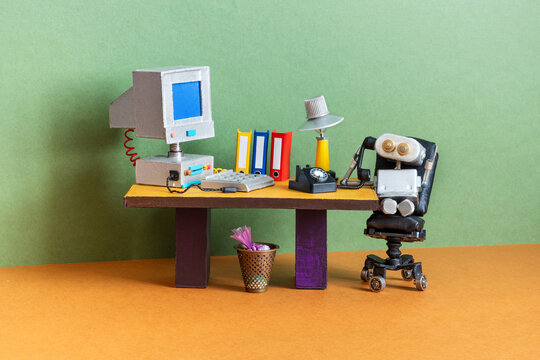 Robot office manager in thought. A toy retro office with a table, books, a personal computer, a desk lamp and a leather armchair.