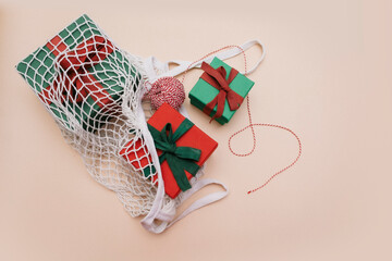 Gifts with ribbons and a skein of red and white rope lie in a white eco-friendly string bag on a beige background. Top view. Copy space