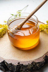 jar of honey and honey dipper on a light background, top view.