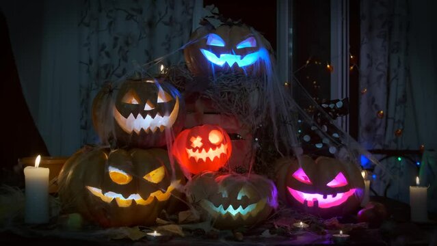 Holiday lanterns made of carved pumpkins, placed in a pile, glow with multi-colored lights in the smoke in the dark. Halloween background.