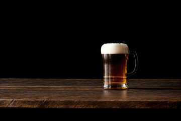 glass of beer on wooden table isolated on black background with copy space - obrazy, fototapety, plakaty