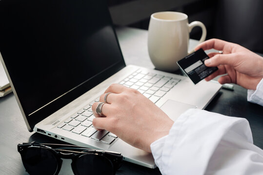 Elegantly poised, a woman's hands gracefully utilize a laptop and credit card for seamless online shopping, epitomizing the essence of modern e-commerce. Online shopping concept