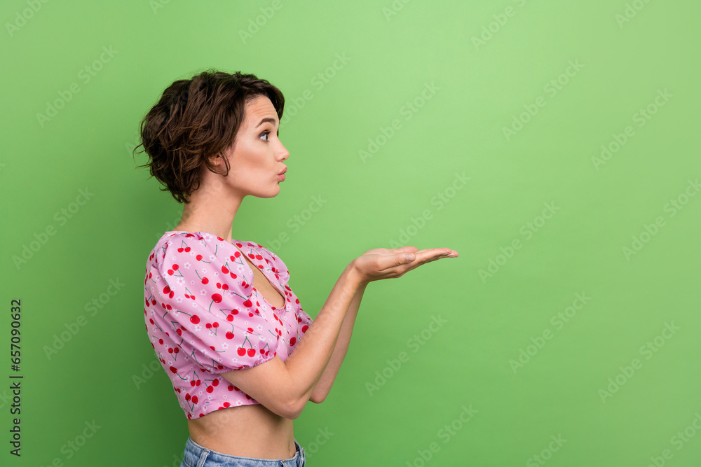 Poster Photo of flirty sweet girl dressed print top sending arms kiss empty space isolated green color background