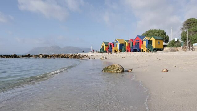 Rainbow colored beach huts overlook gentle waves lapping on beach sand