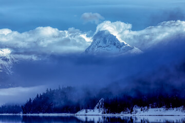 winter scene of a majestic mountain peak shrouded in fog above Lake McDonald, Glacier National Park, Montana