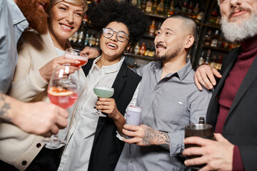 smiling multiethnic colleagues holding glasses with alcohol drinks while spending time in bar