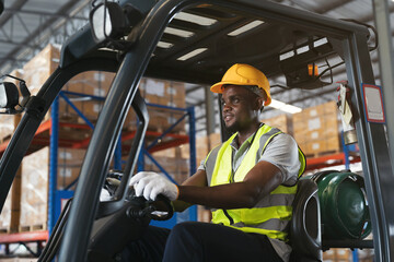 African American male warehouse worker in safety vest and helmet driving and operating on forklift truck for transfer products or parcel goods in the industrial storage warehouse © amorn