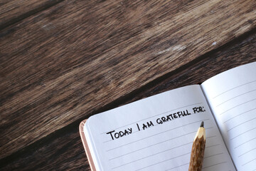 Open journal with handwritten text for gratitude and thanksgiving and pencil on wooden table. Top...