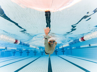 Underwater frontal photo of an adult male with an amputated arm swimming in an indoor pool....